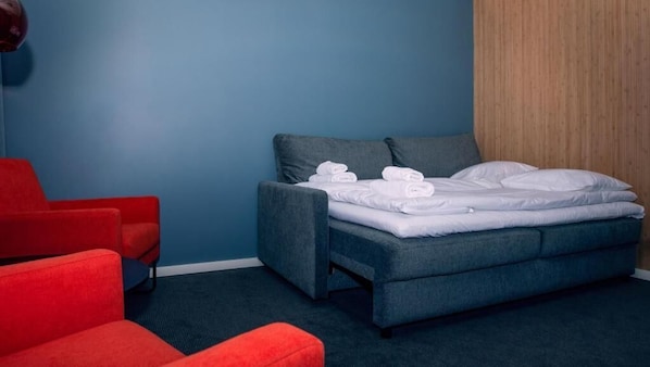 A modern hotel room with a blue wall, a grey sofa, and a bed with white linens. - Narvik Hotel Wivel (Narvik)