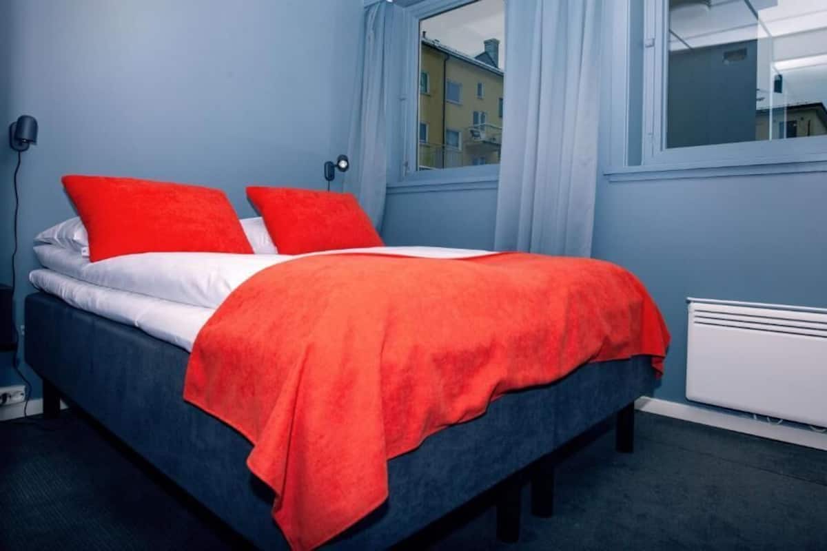 A bed with a red blanket and pillows, a white mattress, and a blue headboard.