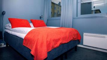Una cama con una colcha roja, almohadas y un cabecero azul.