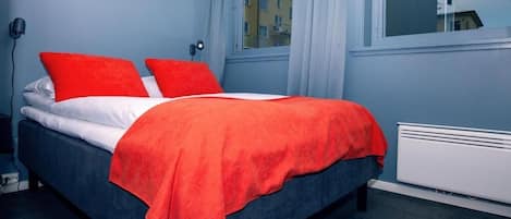 A bed with a red blanket and pillows, a white mattress, and a blue headboard.