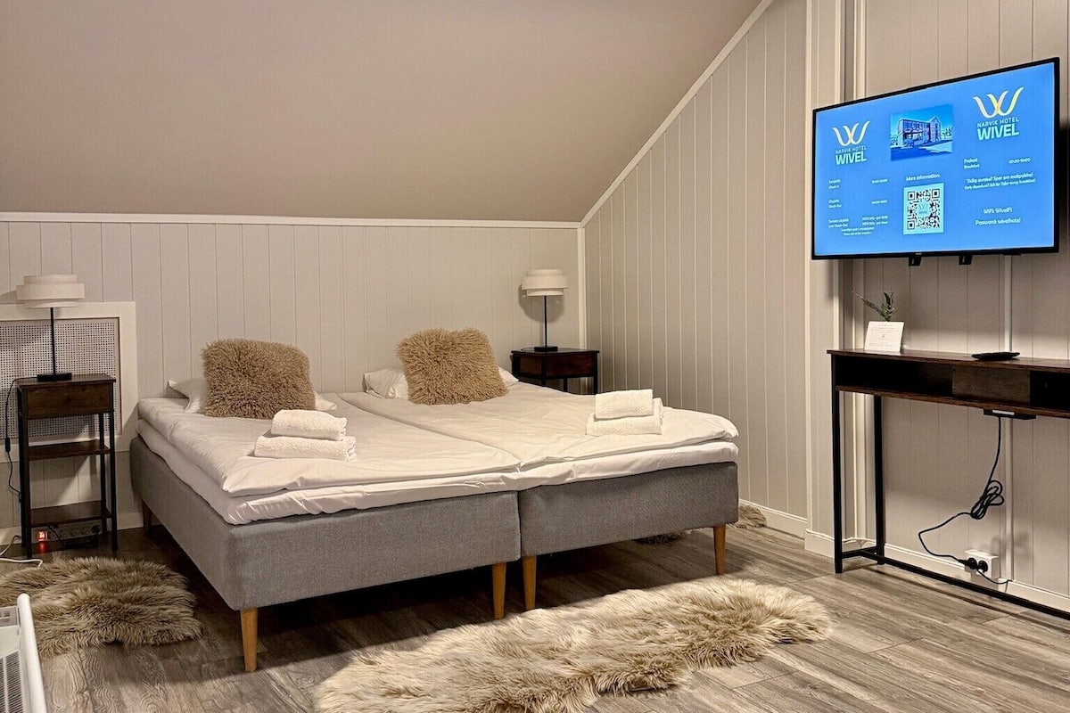 A modern bedroom with a bed, a TV, and a wooden floor.