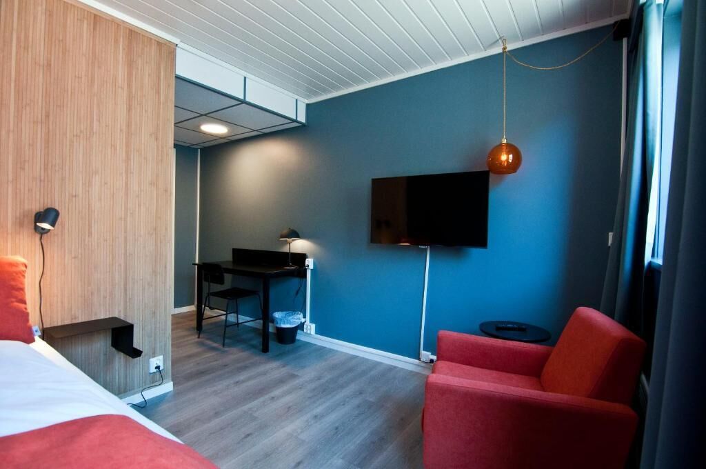 Een hotelkamer met een bed, een bureau, een stoel, een televisie en een rode fauteuil.