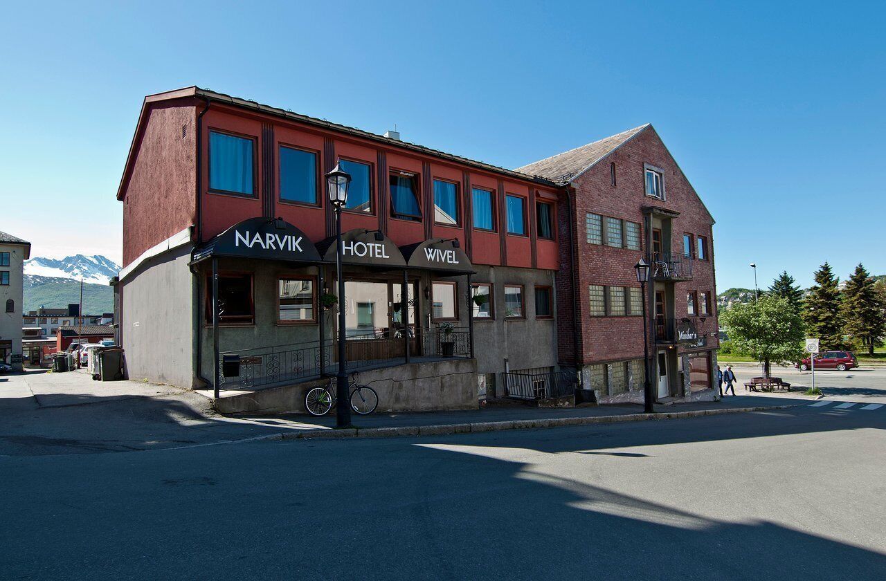 A two-story building with a red facade, labeled as 'NARVIK HOTEL WIEL' with a balcony on the second floor.