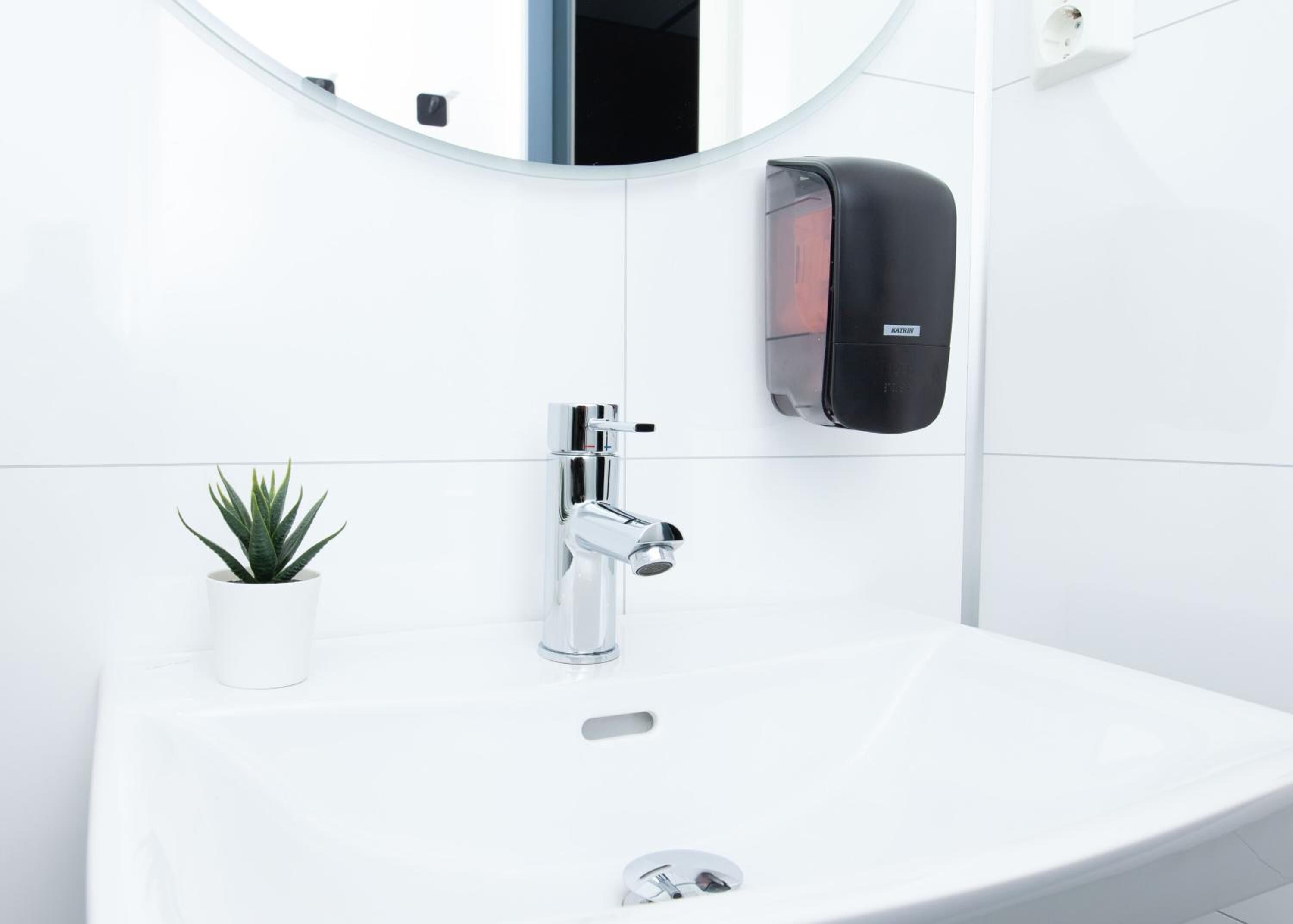 A modern bathroom with a white sink, chrome faucet, and a round mirror.
