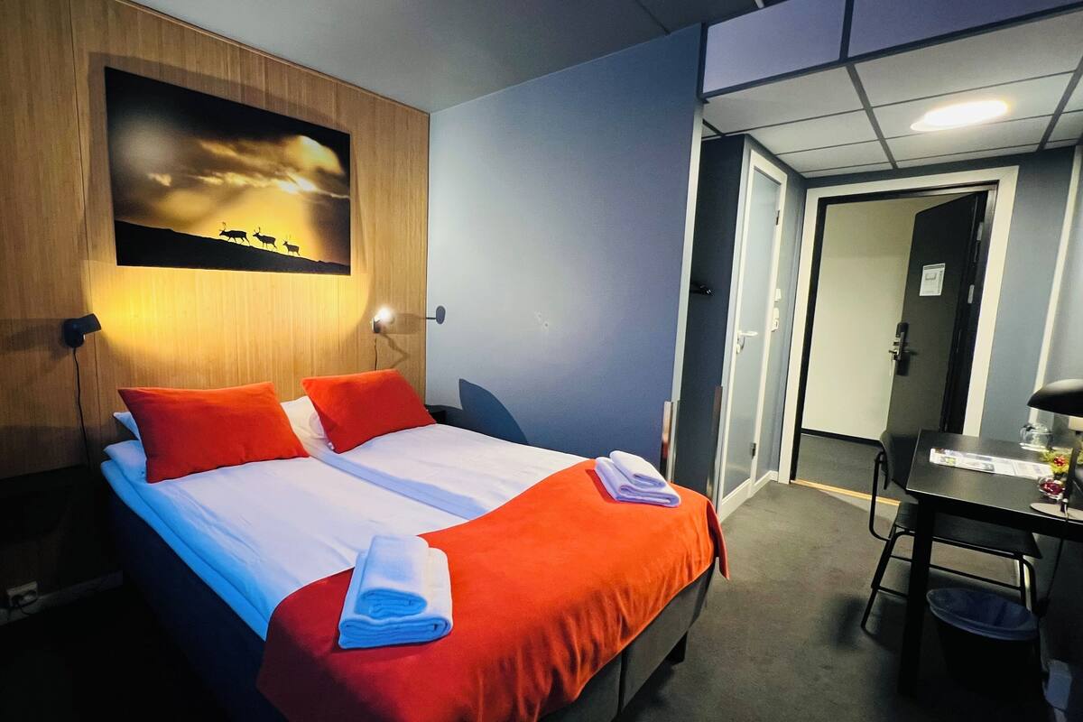 A hotel room with a bed, a desk, and a door.