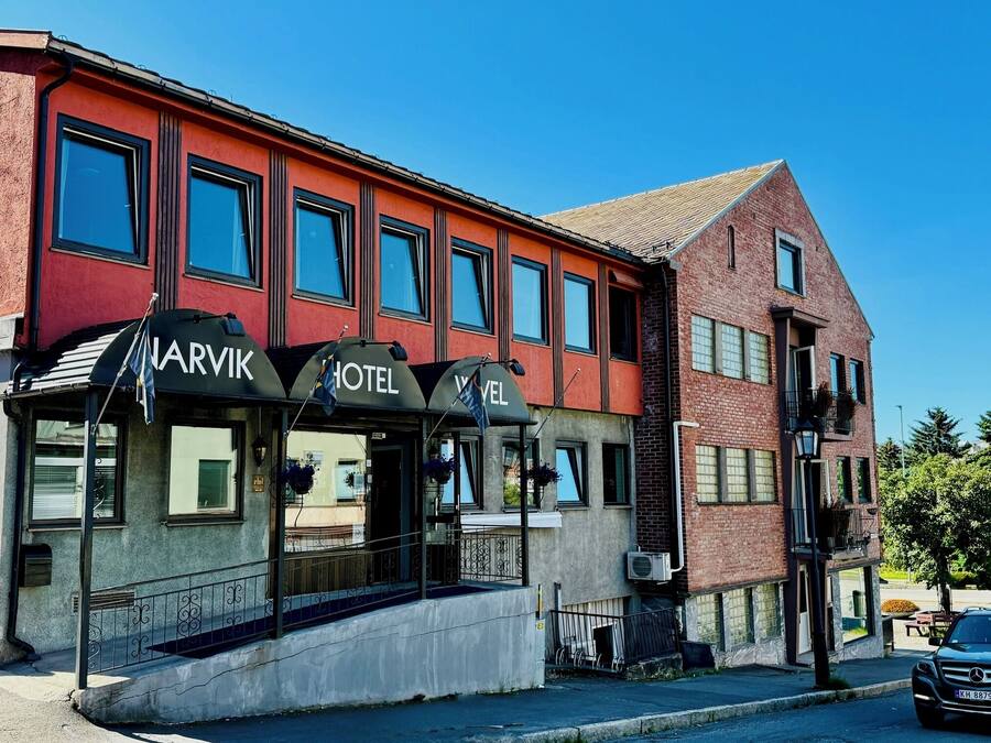 Ett hotell med en röd fasad, många fönster och ett svart markis med namnet ”NARVIK HOTEL”.