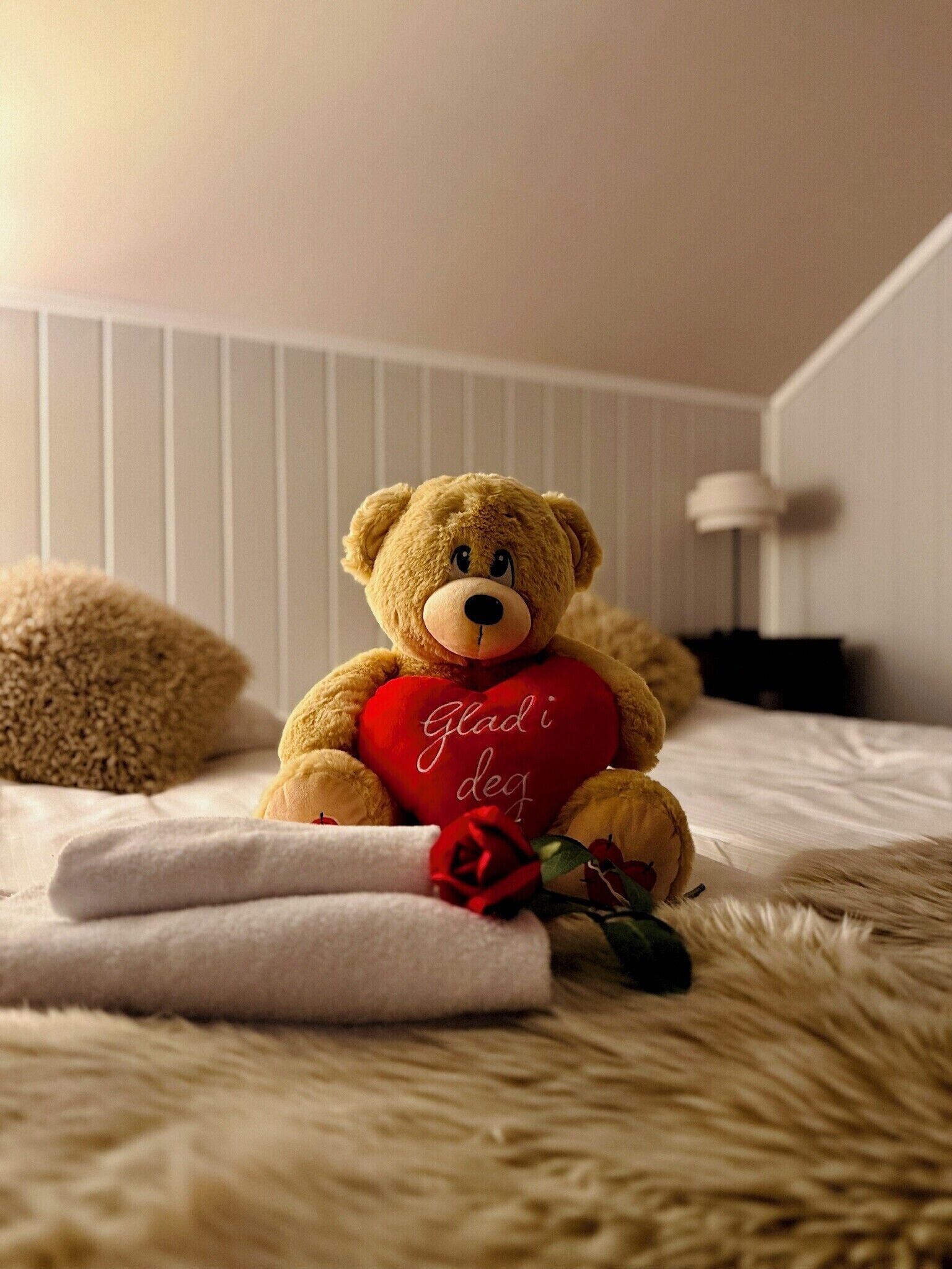 A teddy bear with a heart-shaped pillow on a bed.