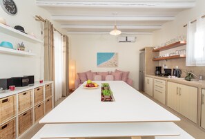 A modern kitchen with a white table, wicker baskets, a fruit bowl, and a plant centerpiece.