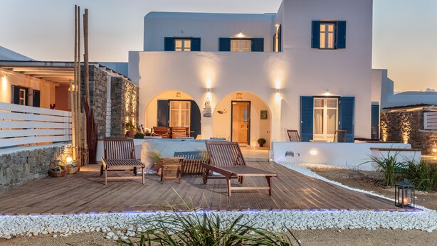 Un edificio moderno con fachada blanca, contraventanas azules y una terraza de madera con asientos.
