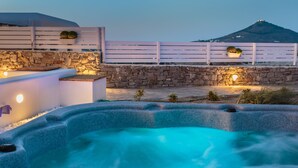 Un área de hidromasaje con paredes de piedra y terraza de madera, con vistas a un paisaje montañoso.