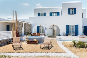 A white building with blue shutters, a wooden deck with lounge chairs, and a hot tub.