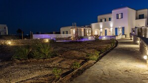 Un sendero bien iluminado que conduce a un edificio con un muro de piedra y un jardín con plantas.