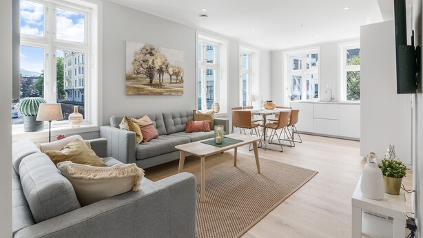 A modern living room with a grey sofa, a coffee table, and a dining area with a table and chairs. - Barfot Apartments (Bergen)