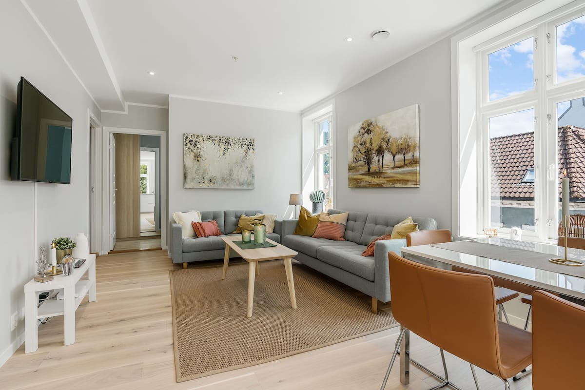 A modern living room with a grey sofa, a coffee table, and a dining area with a glass table and chairs.