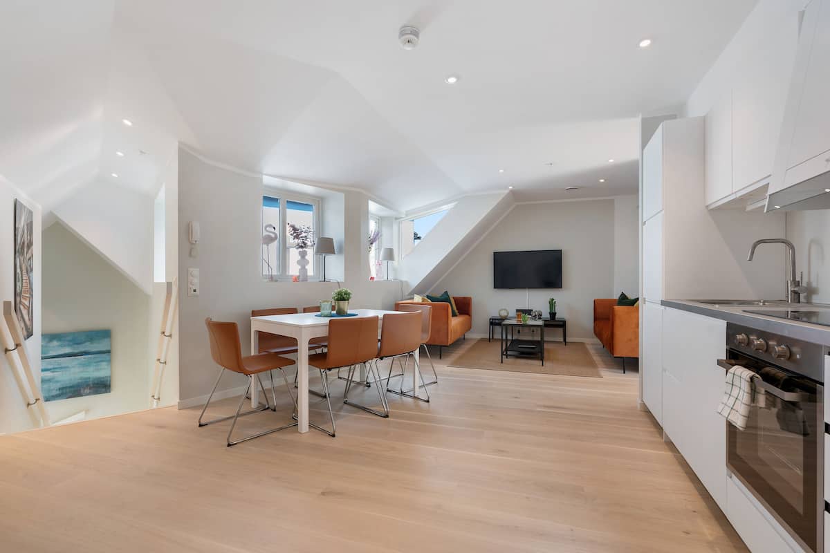 A modern kitchen with a dining area, a TV, and a staircase.