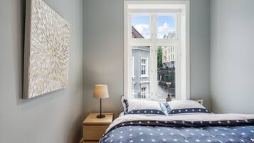 A bedroom with a bed, a nightstand, a lamp, and a window with a view of buildings.