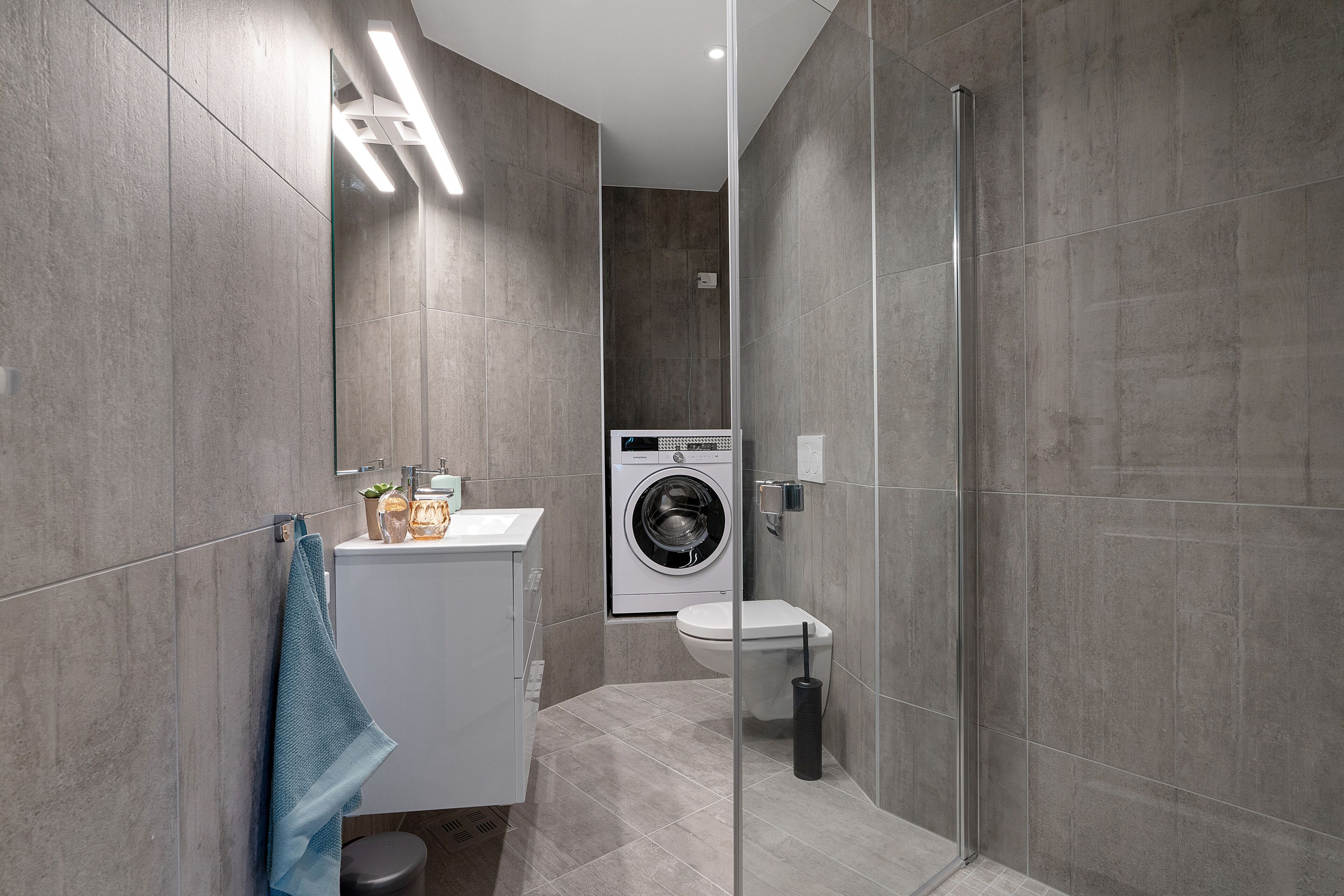 Ein modernes Badezimmer mit Waschmaschine, Toilette und einer Duschkabine aus Glas.