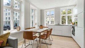 A modern kitchen with a dining area, large windows, and a view of the city. - Barfot Apartments (Bergen)