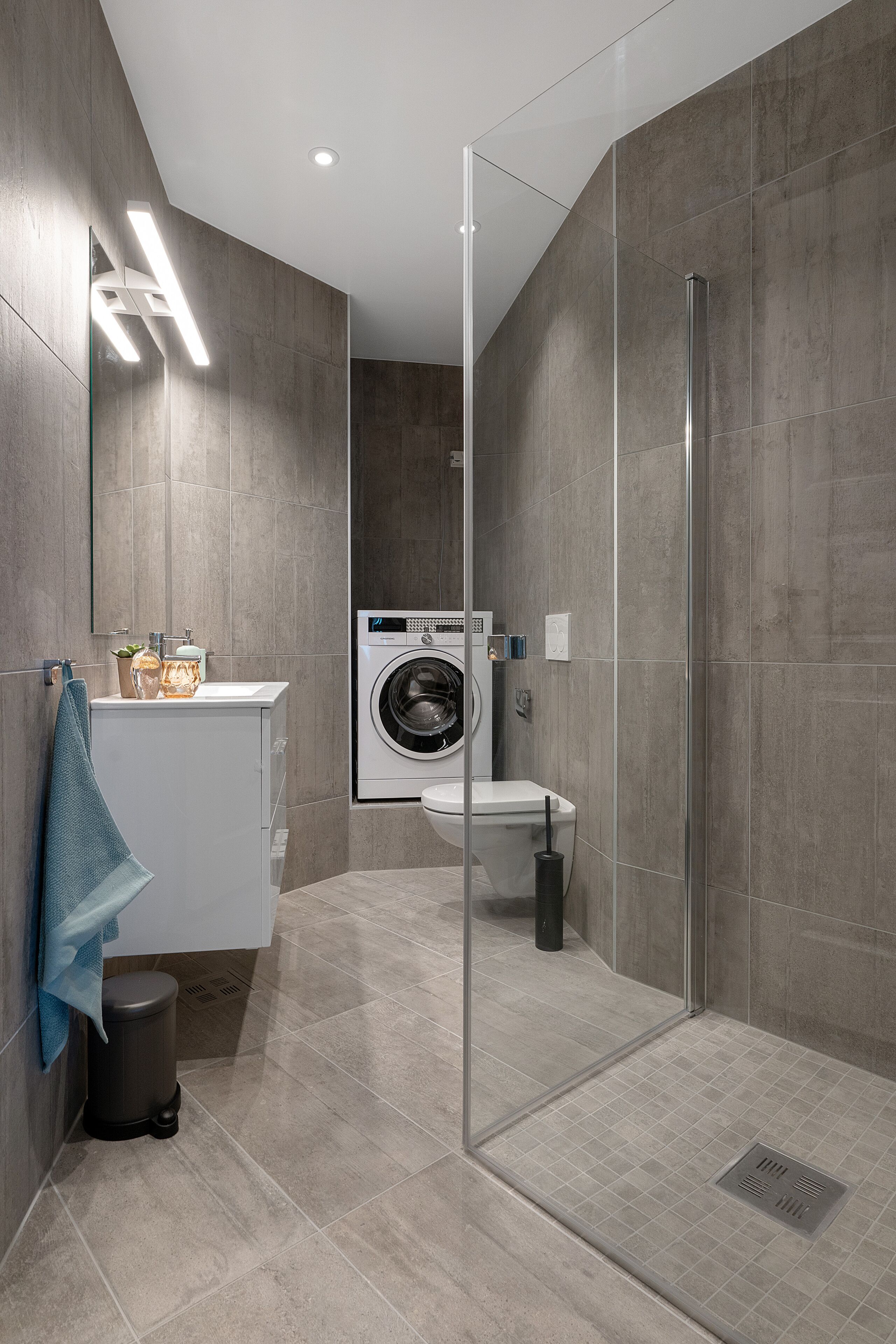 A modern bathroom with a glass shower enclosure, a washing machine, and a sink with a towel.
