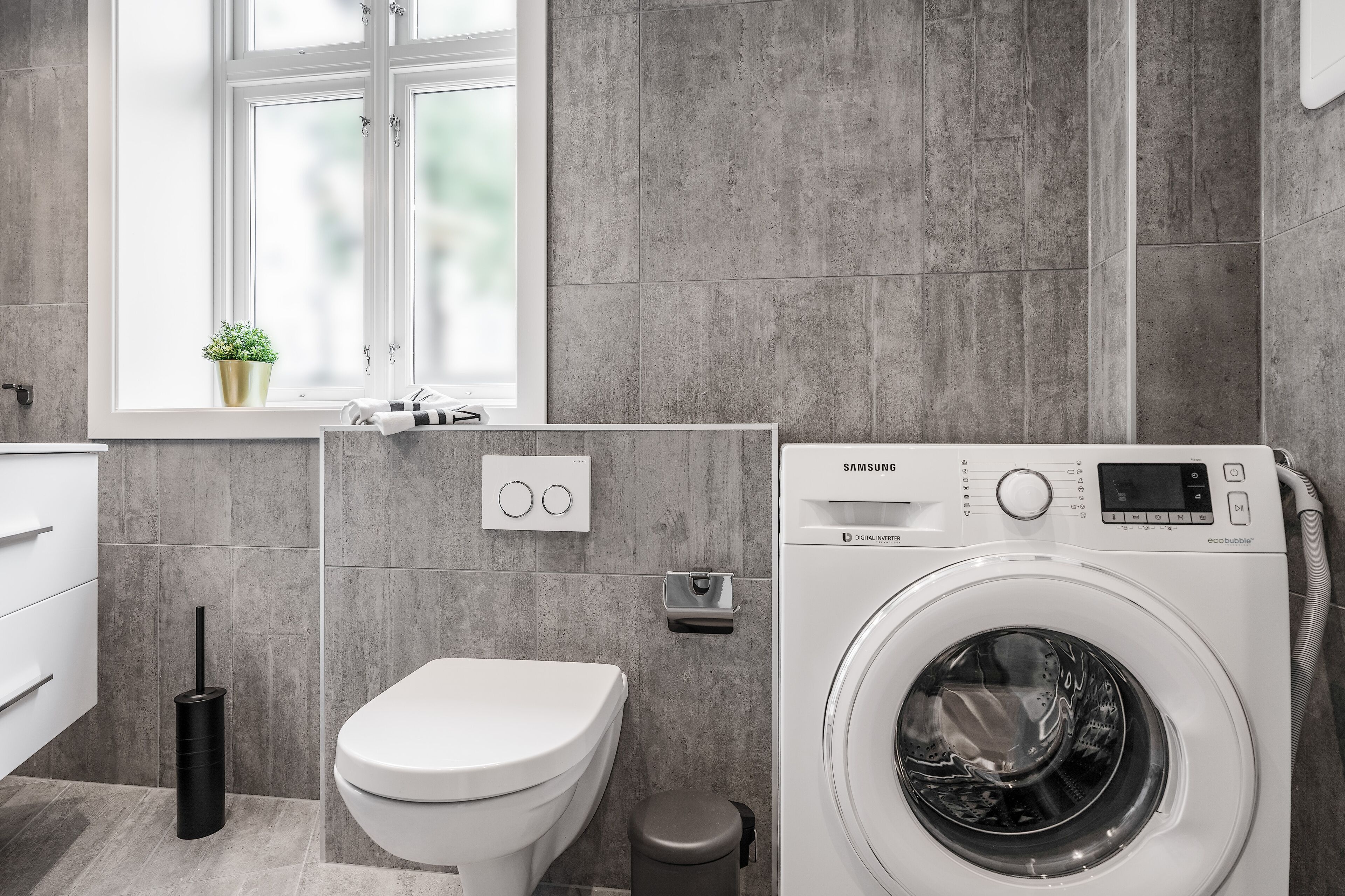 Un baño moderno con lavadora, inodoro y una ventana con una planta.