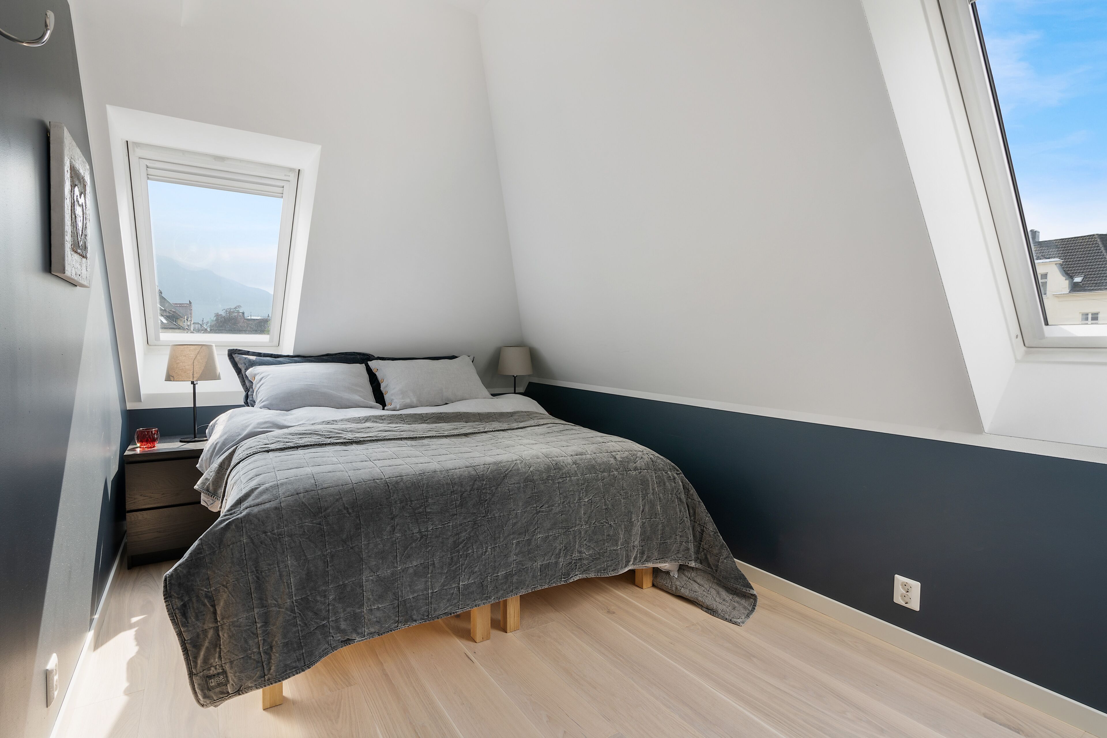 Un dormitorio con cama, mesitas de noche, ventana y vistas a edificios.