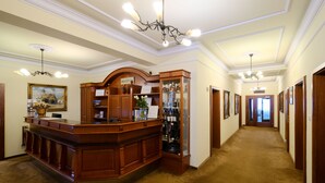 A reception area with a wooden desk, a reception sign, a framed picture on the wall, and a chandelier. - Garni hotel Matysak (Bratislava)