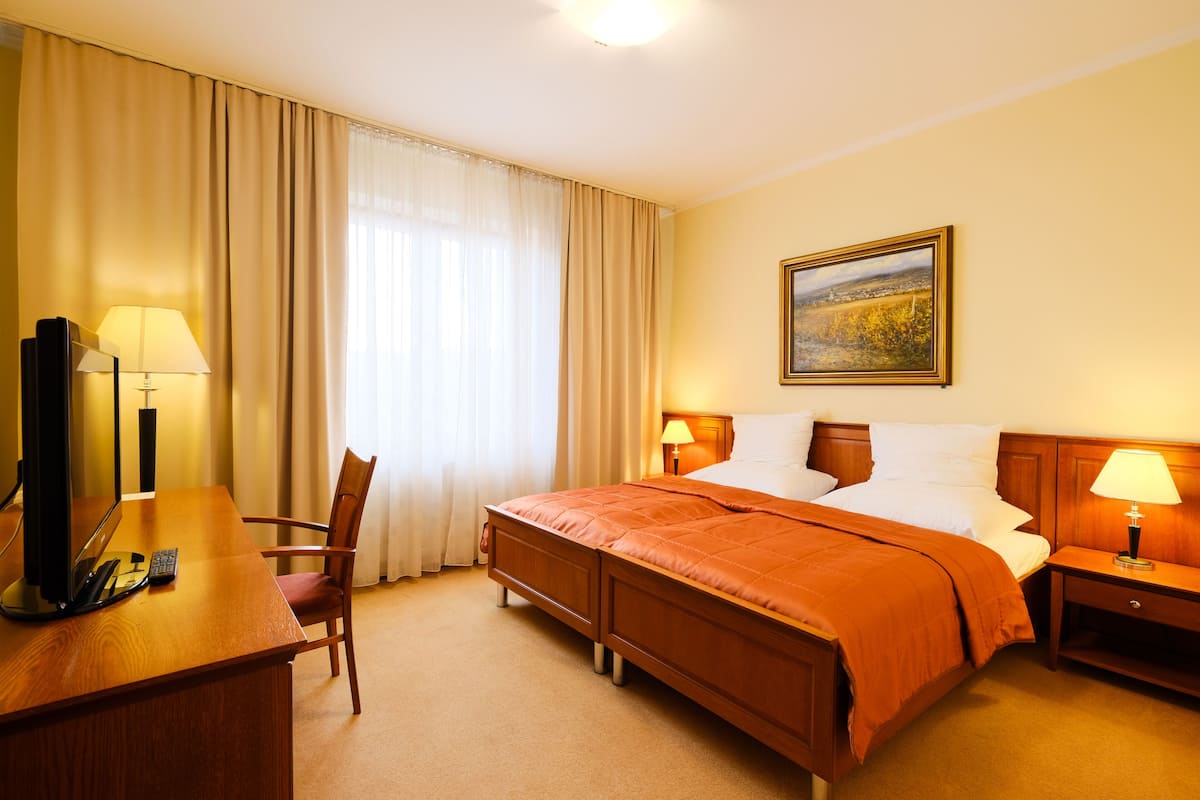 A hotel room with a bed, a desk, a chair, a television, and two lamps.