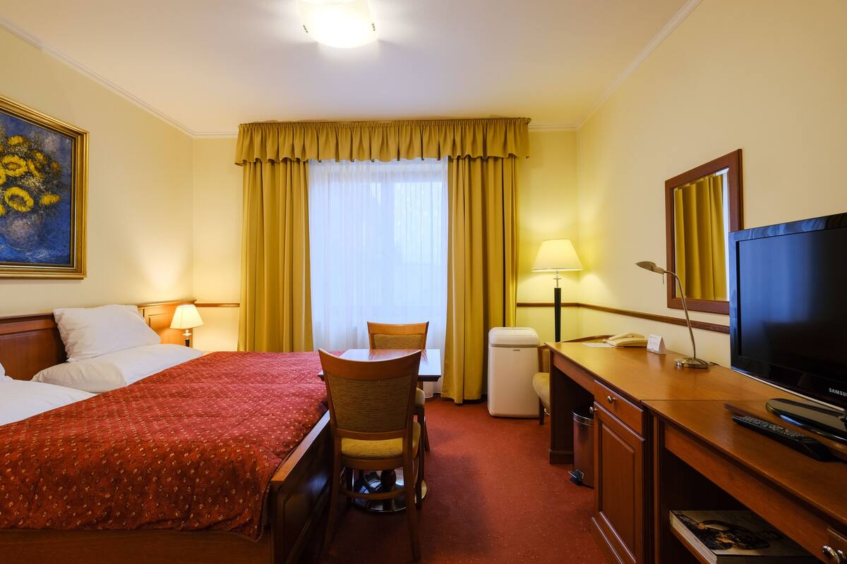 A hotel room with a large bed, a desk with a chair, a television, and a painting on the wall.