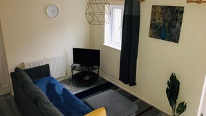 Una sala de estar con un sofá, un televisor, una ventana con cortinas, un reloj de pared y un cuadro.