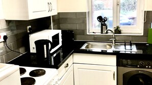 Una cocina compacta con armarios blancos, estufa, lavaplatos y pileta.