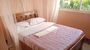 Un lit bien fait, avec une tête de lit en bois, une couvre-lit rose et des oreillers blancs.