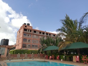 A hotel with a swimming pool, red chairs, and palm trees. - Dillions Highway Motel (Kilimambogo)