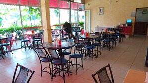 Un vaste espace de restauration intérieur, doté de nombreuses tables et chaises, de grandes fenêtres surmontées d’auvents rouges et offrant une vue dégagée sur l’extérieur.