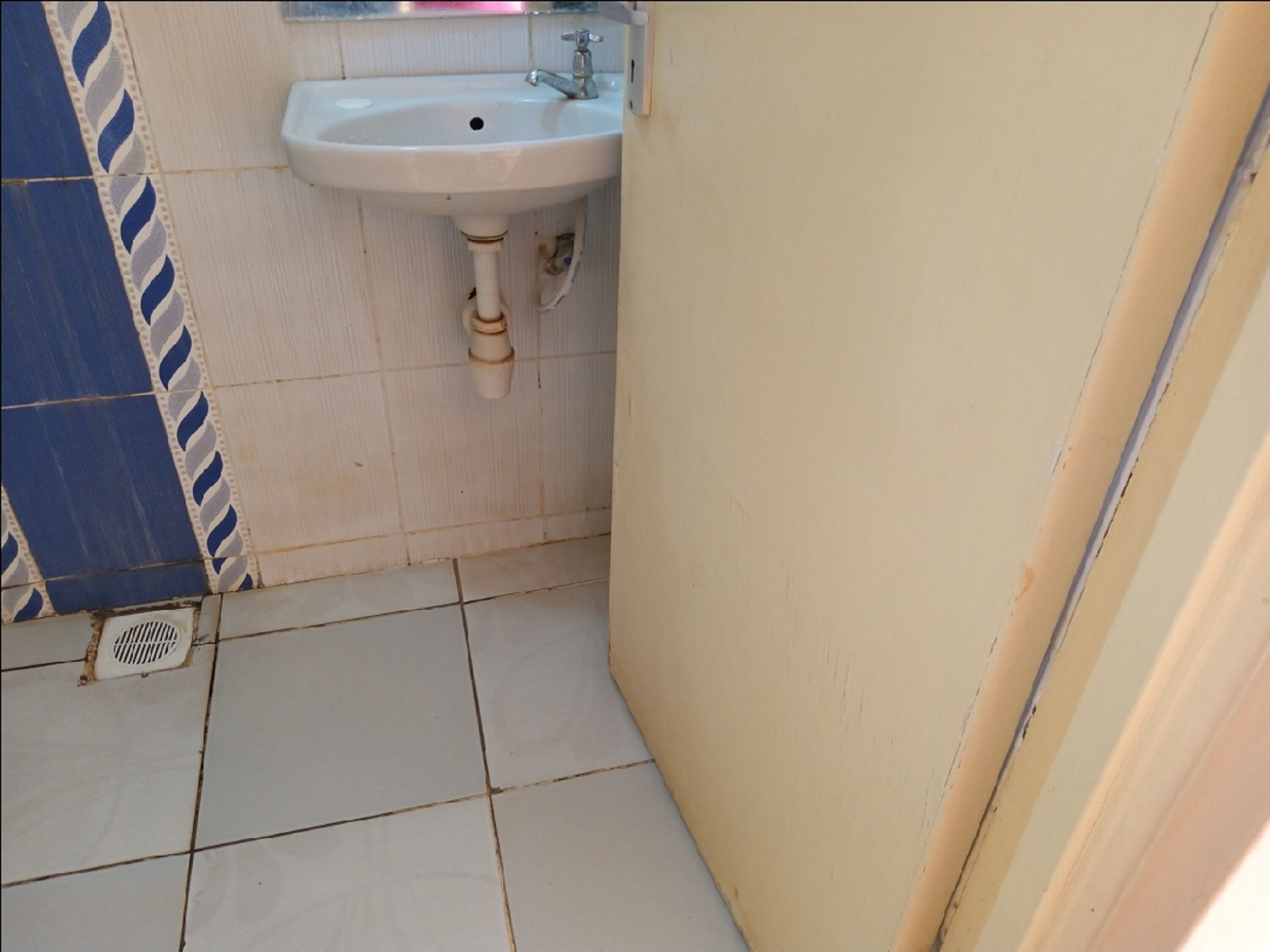 Un baño pequeño con un lavamanos blanco, una pared con azulejos blancos y azules, y un piso con pisos blancos.