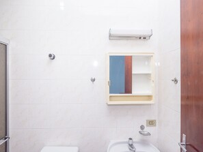 A bathroom with white tiles, a sink, a mirror, and a shower. - Hostel Suarão (Itanhaém)