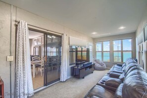 A living room with a sliding glass door leading to a balcony, a dark leather sofa, a flat-screen TV, and a dining area visible through the glass. - CL 1683 Our Lake View (Canyon Lake)