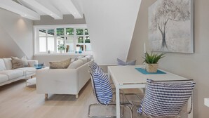 A modern living room with a white sofa, a dining table with chairs, and a large window offering a view of greenery outside. - Fosswinckel Apartments (Bergen)