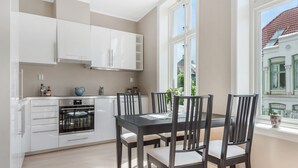 A modern kitchen with white cabinets, a black dining table, and chairs. There is a window with a view of buildings outside. - Fosswinckel Apartments (Bergen)