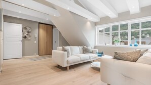 A spacious living area with a white sofa, a coffee table, and a view of a green landscape through large windows. - Fosswinckel Apartments (Bergen)