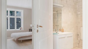 A bedroom with a bed, a window, and a bathroom with a sink and mirror. - Fosswinckel Apartments (Bergen)