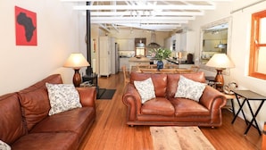 A living room with two brown leather sofas, a wooden coffee table, and a kitchen in the background. - Lime Cottage (Bel Ombre)