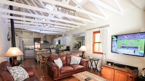 A spacious living room with a brown leather sofa, a wooden coffee table, and a television mounted on the wall. - Lime Cottage (Bel Ombre)