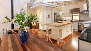 A modern kitchen with white cabinetry, a central island, and a dining area with a wooden table and chairs. - Lime Cottage (Bel Ombre)