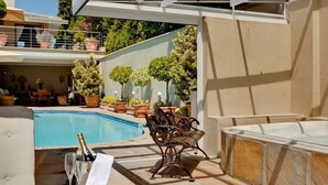 A poolside area with a hot tub, lounge chairs, and a table with a bottle of champagne. - Lime Cottage (Bel Ombre)