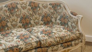 Un canapé ancien à motifs floraux, doté de pieds décoratifs, est placé dans une pièce où un tableau encadré orne le mur.