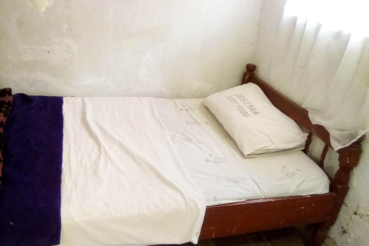 A small, single-bed room with a wooden frame, white bedding, and a pillow labeled "OSLEMIA GUEST HOUSE".