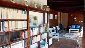 A cozy living room with a bookshelf, a white armchair, a sofa, and a coffee table. - Posada La Vieja Escuela (San Vicente de la Barquera)