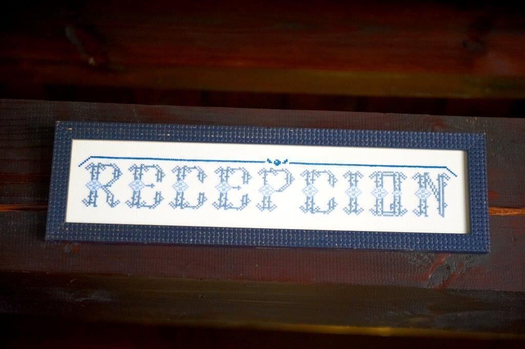 Un letrero con la palabra 'RECEPTION' en un diseño de punto de cruz.