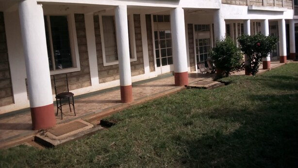 Un edificio con un porche cubierto, columnas y una pequeña zona de estar con una silla.
