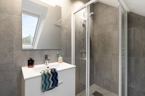 Un baño moderno con ducha, lavabo y espejo, y una toalla colgada en la pared.